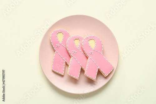 Plate with cookies in shape of pink ribbon on light yellow background. Breast cancer awareness concept