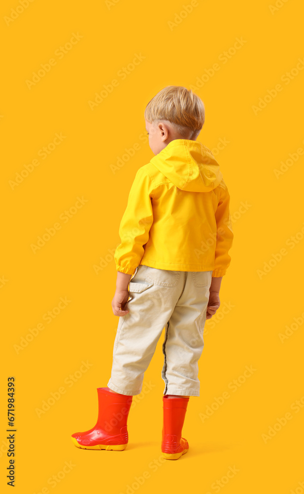 Little boy in rubber boots on yellow background, back view Little boy in rubber boots on yellow background, back view