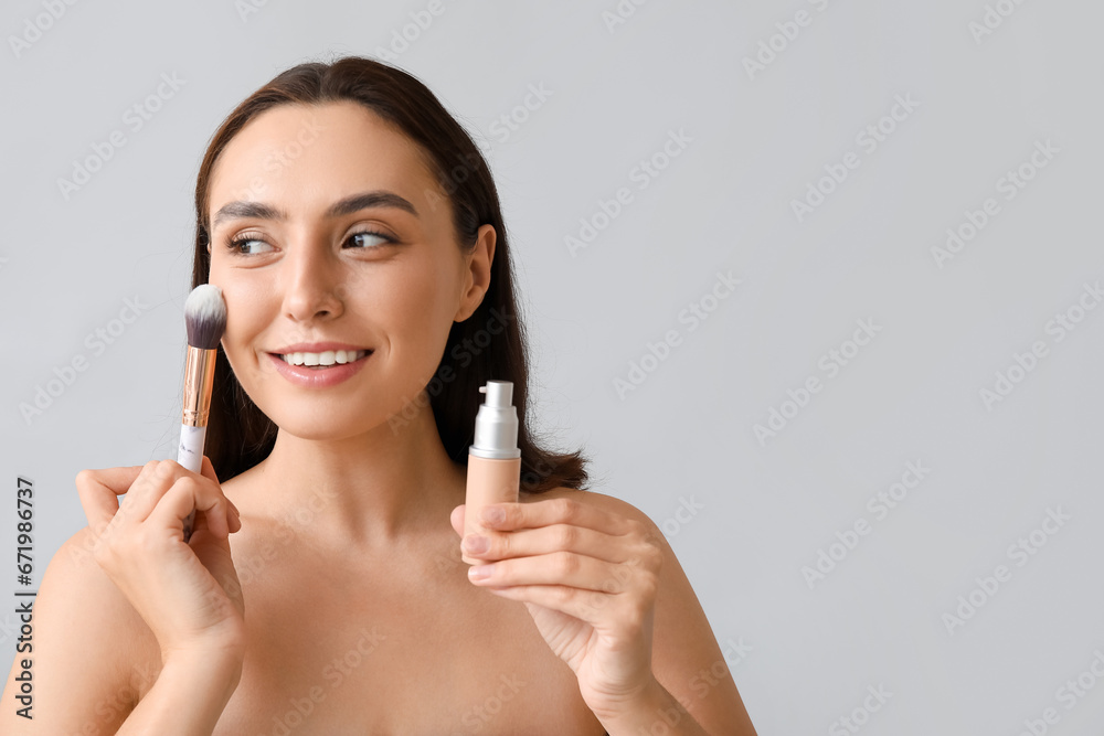 Young woman with makeup foundation and brush on light background, closeup Young woman with makeup foundation and brush on light background, closeup
