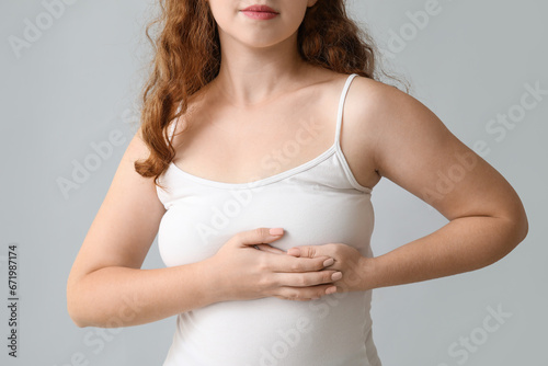 Young woman checking her breast on light background, closeup. Cancer awareness concept