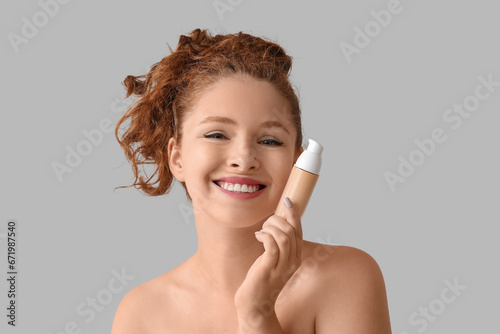 Young redhead woman with makeup foundation on light background, closeup