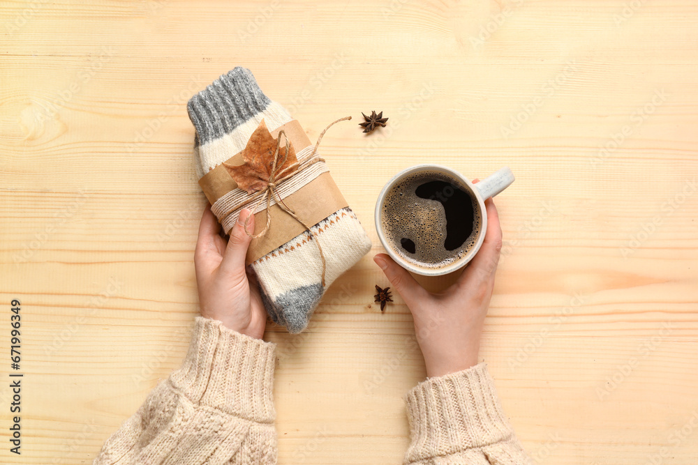 Woman with cup of coffee and warm socks on beige wooden background