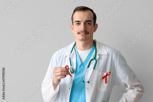 Young male doctor with red ribbons on grey background. World AIDS Day concept © Pixel-Shot