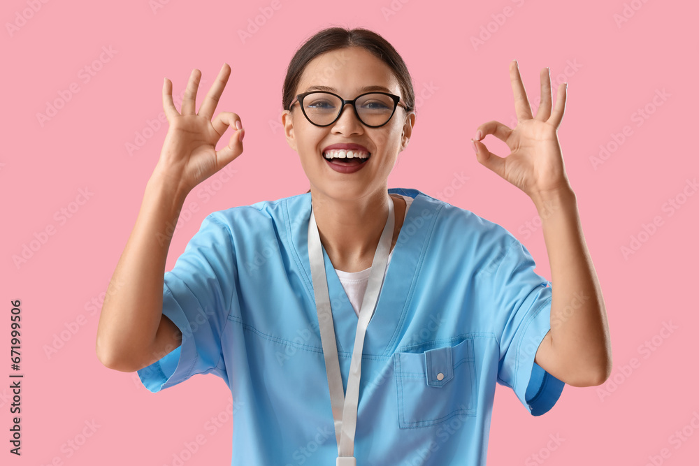 Asian medical intern showing OK on pink background Asian medical intern showing OK on pink background