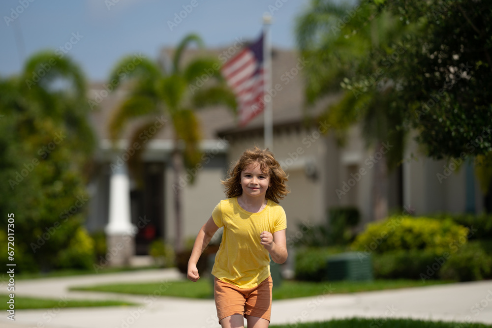 Cute kid boy running across american neighborhood street. Summer, childhood, leisure and people concept. Happy little blonde child boy running in summer park outdoor. Sport and run.