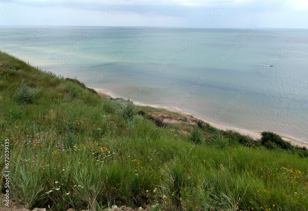 Azov sea coastal area with smooth green grass slope. Seashore view with blue sky horizon. Azov sea coastal area with smooth green grass slope. Seashore view with blue sky horizon.