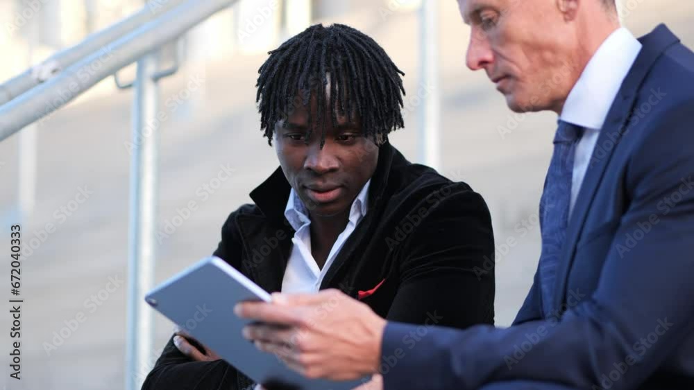 Business professionals engage in conversation while seated on the staircase with a tablet Business professionals engage in conversation while seated on the staircase with a tablet