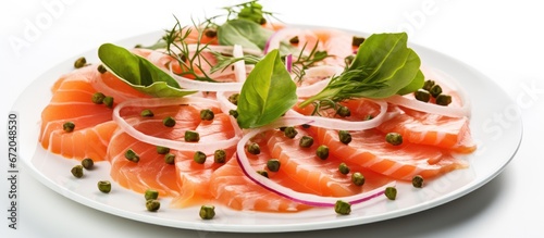On a plain white background there is a tasty salmon carpaccio adorned with capers basil and onion