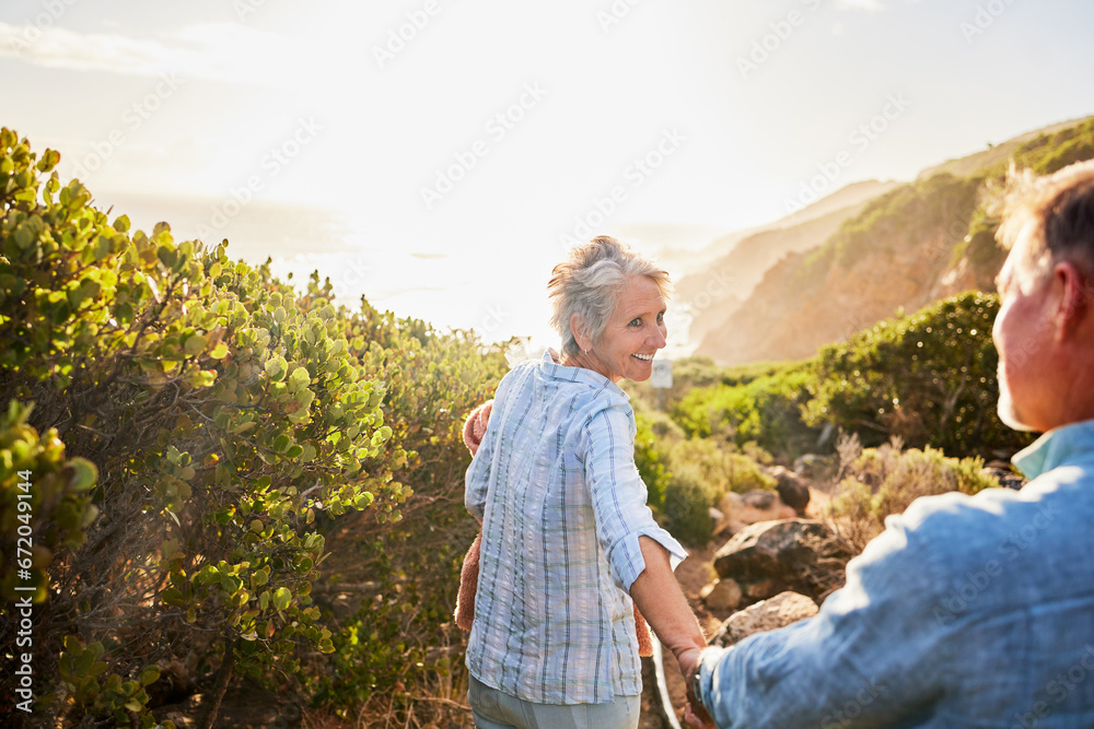 Naklejka premium Love, holding hands and nature, senior couple walking with picnic blanket for romance and valentines day. Green mountain path, old man and woman on walk or hike for romantic valentine date at sunset.