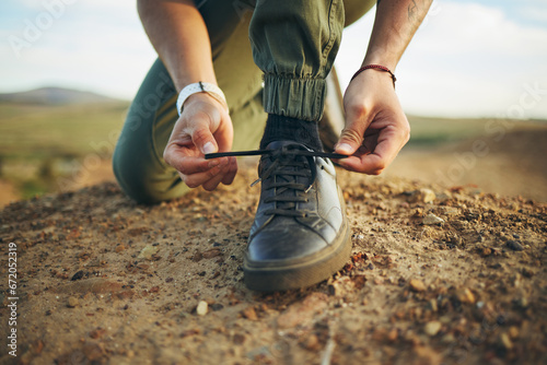 Hands, tie shoes and hiking in nature for travel, training or adventure outdoor. Fitness, sports and person tying laces on sneakers to start workout, walk or running, cardio or workout in countryside photo