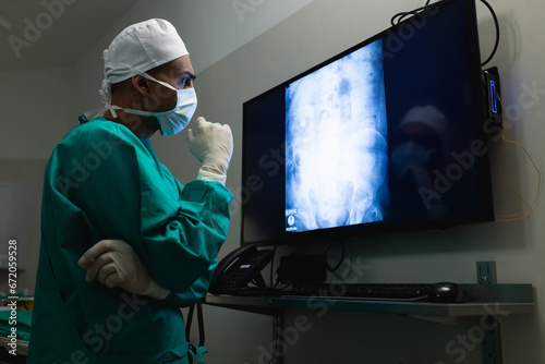 Biracial male surgeon looking at x-ray scans on screen in operating theatre at hospital photo