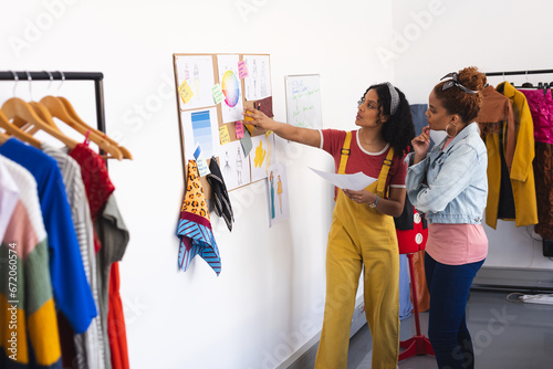 Two biracial female fashion designers discussing and looking at colour wheel in sunny studio photo