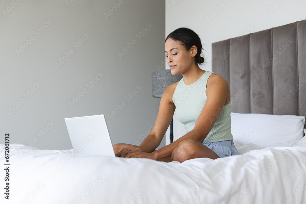 Happy biracial woman using laptop and sitting in bedroom Happy biracial woman using laptop and sitting in bedroom