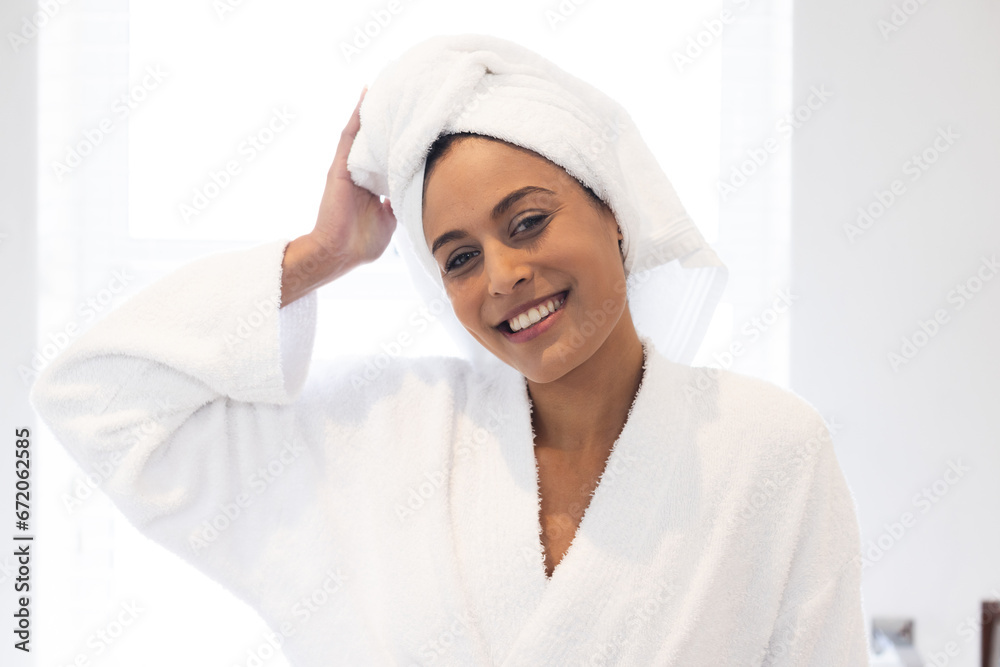 Portrait of happy biracial woman wearing white bathrobe and towel on head in bathroom Portrait of happy biracial woman wearing white bathrobe and towel on head in bathroom