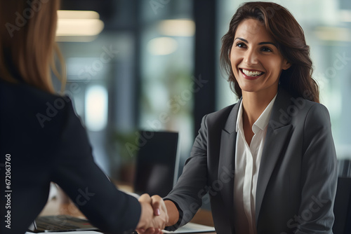 Happy mid aged business woman manager handshaking greeting client in office. Smiling female executive making successful deal with partner shaking hand at work standing at meeting table