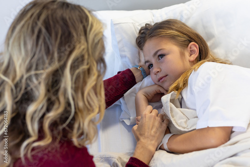 Caucasian mother holding hand of sick daughter patient lying in hospital bed photo