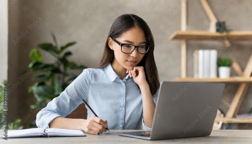 Young busy serious Asian business woman manager using laptop and mobile cell phone devices in office. Professional female executive holding smartphone, working on cellphone sitting at desk Young busy serious Asian business woman manager using laptop and mobile cell phone devices in office. Professional female executive holding smartphone, working on cellphone sitting at desk