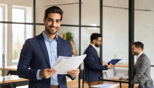 Happy young Latin business man checking financial documents in office. Smiling male professional account manager executive lawyer holding corporate tax bill papers standing at work photo