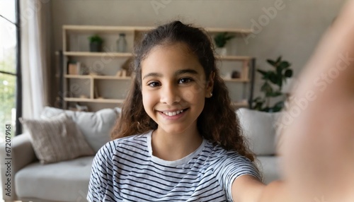Happy pretty hispanic gen z teen girl holding smartphone looking at camera taking selfie shot for social media, making video call at home by virtual mobile app. Close up face headshot portrait photo