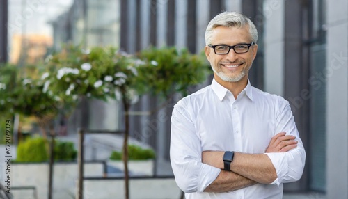 Confident happy mature older business man leader, smiling middle aged senior old professional businessman wearing white shirt glasses crossed arms looking at camera standing outside photo