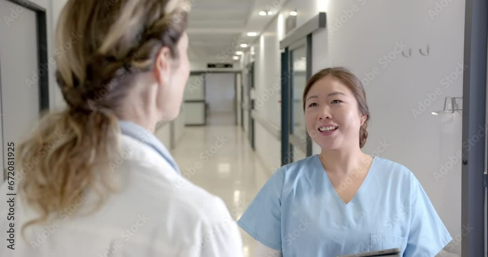 Happy diverse female doctors talking in hospital corridor, turning and smiling, slow motion Happy diverse female doctors talking in hospital corridor, turning and smiling, slow motion