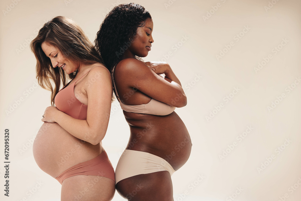 Two pregnant women nurturing their changing bodies with skincare cream - obrazy, fototapety, plakaty 