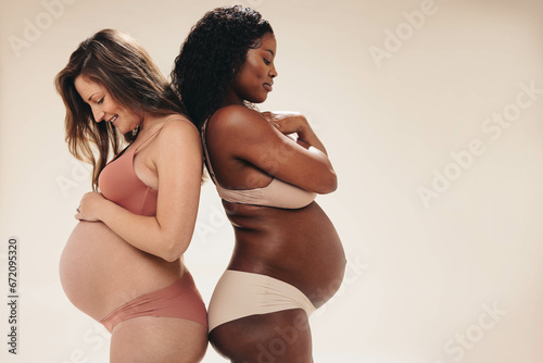 Two pregnant women nurturing their changing bodies with skincare cream photo
