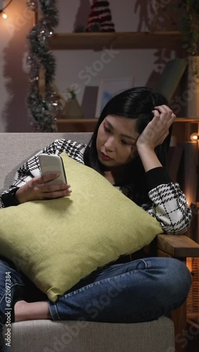 Vertical Screen: asian woman sitting couch in the living room. and addicted to cell phone neglecting her unhappy boyfriend at home in the evening