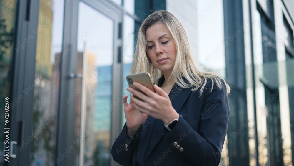 Fototapeta premium Serious confident 40s girl text message. Successful 30s business woman type job sms. Sexy boss lady use mobile cell phone chat close up. Pretty top manager walk. Blond hair person wear city work suit.