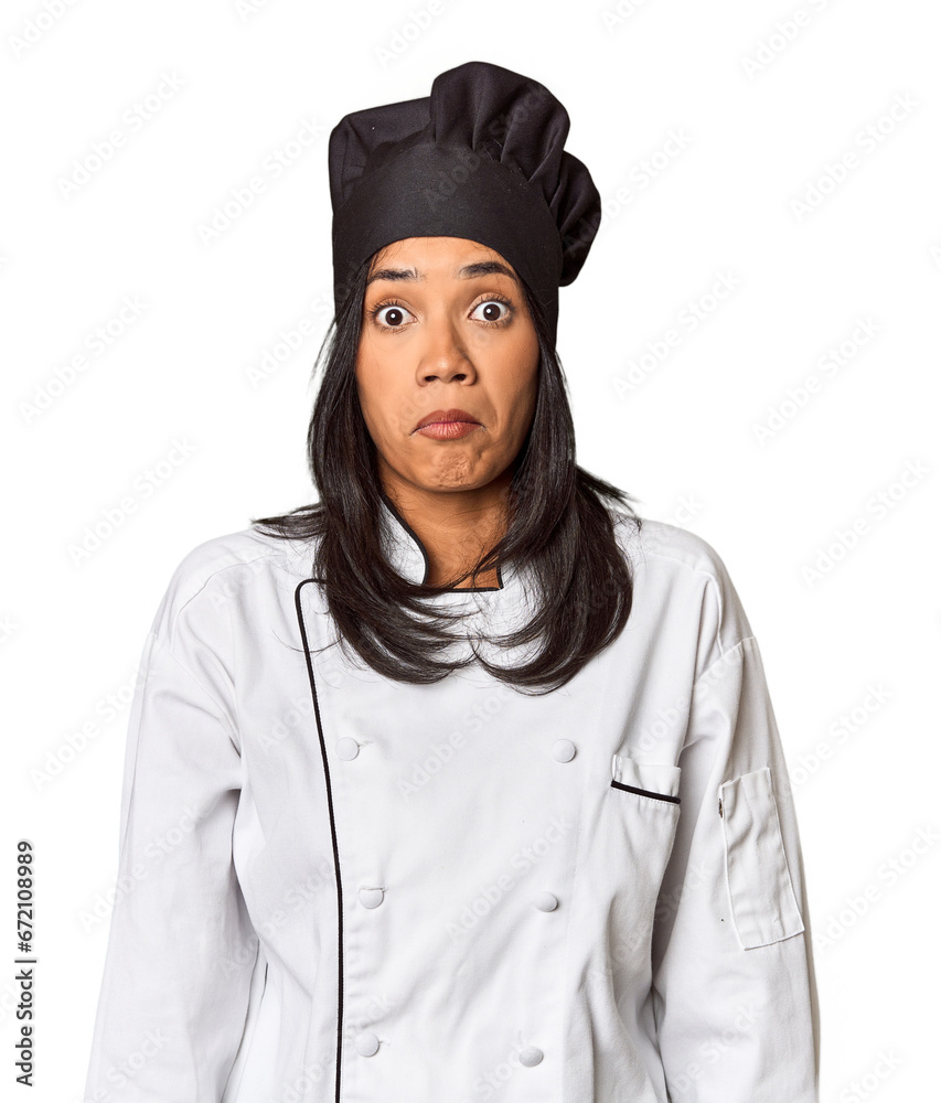 Young Filipina chef with cooking hat in studio shrugs shoulders and open eyes confused.