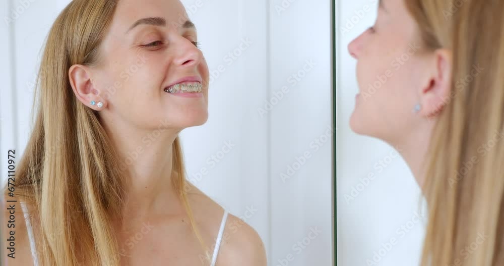 Young woman cheking her new braces in the mirror Young woman cheking her new braces in the mirror