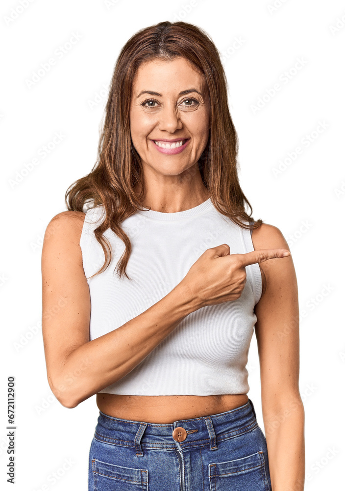 Fototapeta premium Middle-aged woman portrait in studio setting smiling and pointing aside, showing something at blank space.