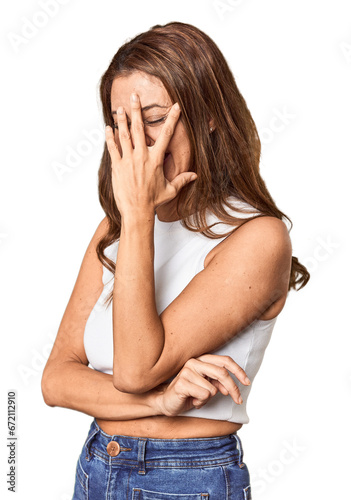 Middle-aged woman portrait in studio setting blink at the camera through fingers, embarrassed covering face.