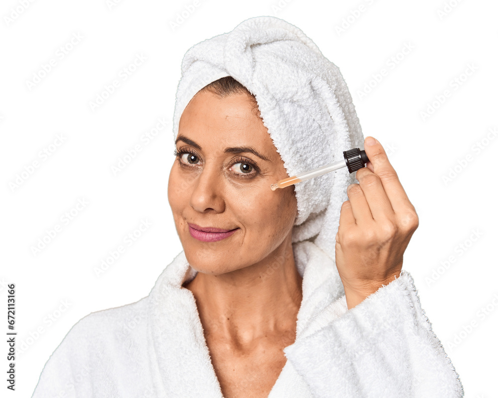 Middle-aged woman applying facial serum in bathrobe in studio Middle-aged woman applying facial serum in bathrobe in studio