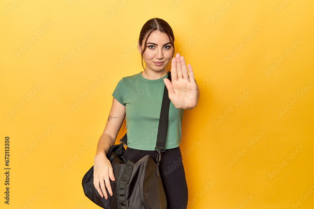 Athletic caucasian woman with sports backpack standing with outstretched hand showing stop sign, preventing you.
