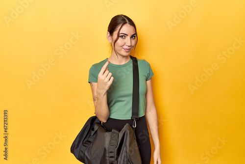 Athletic caucasian woman with sports backpack pointing with finger at you as if inviting come closer.