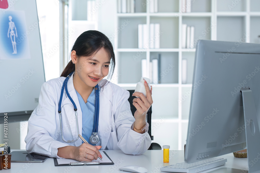 Asian female doctor holding pill bottle in hand, writing prescription, sitting at prescription table, pharmaceutical concept. Asian female doctor holding pill bottle in hand, writing prescription, sitting at prescription table, pharmaceutical concept.
