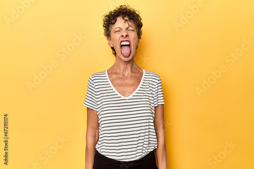 Mid-aged caucasian woman on vibrant yellow funny and friendly sticking out tongue. photo