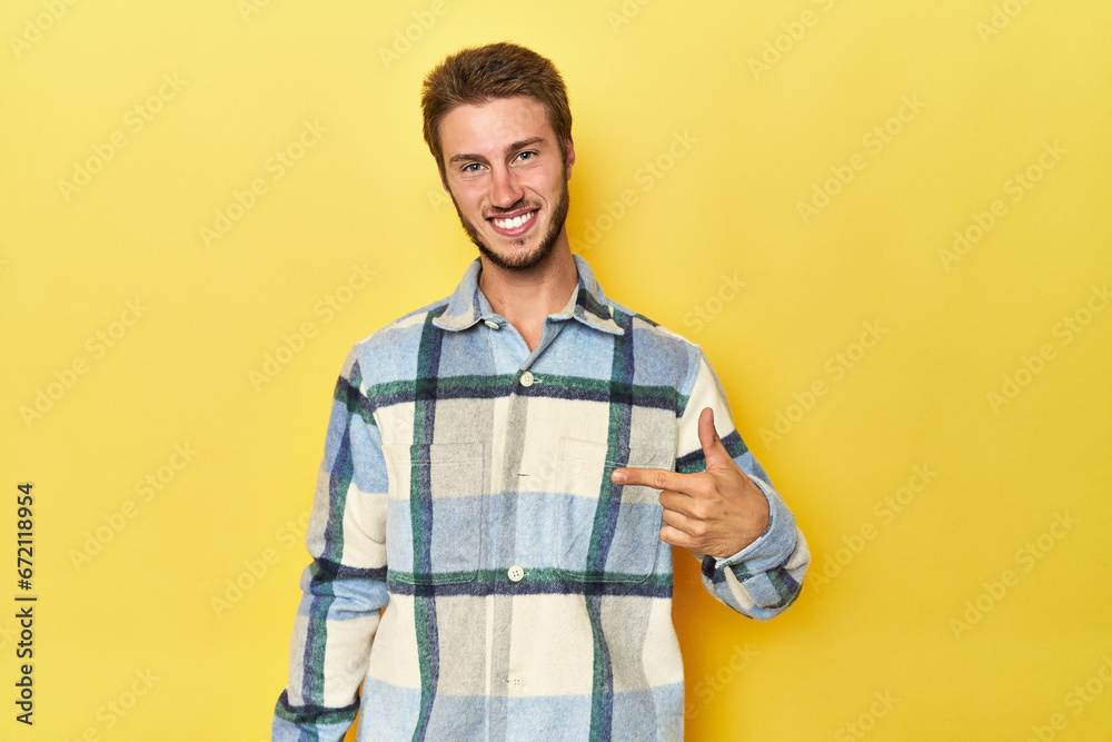 Young Caucasian man on a yellow studio background person pointing by hand to a shirt copy space, proud and confident Young Caucasian man on a yellow studio background person pointing by hand to a shirt copy space, proud and confident