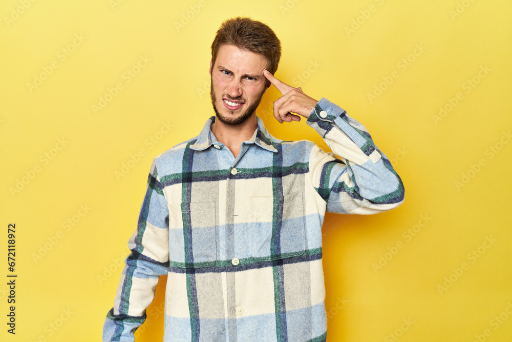 Young Caucasian man on a yellow studio background showing a disappointment gesture with forefinger.