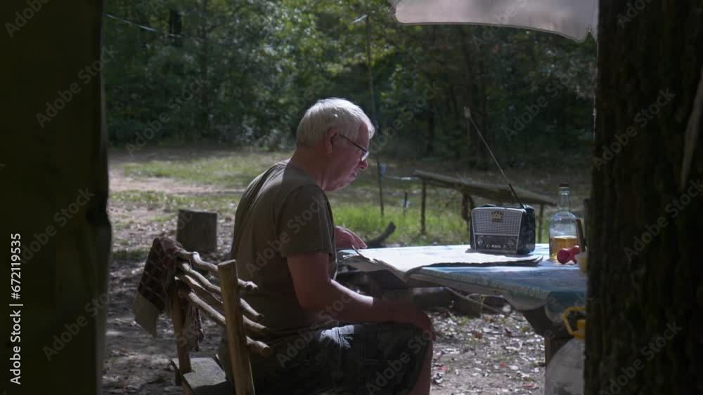 Man tunes in small portable radio when reading newspaper woodland setting Man tunes in small portable radio when reading newspaper woodland setting