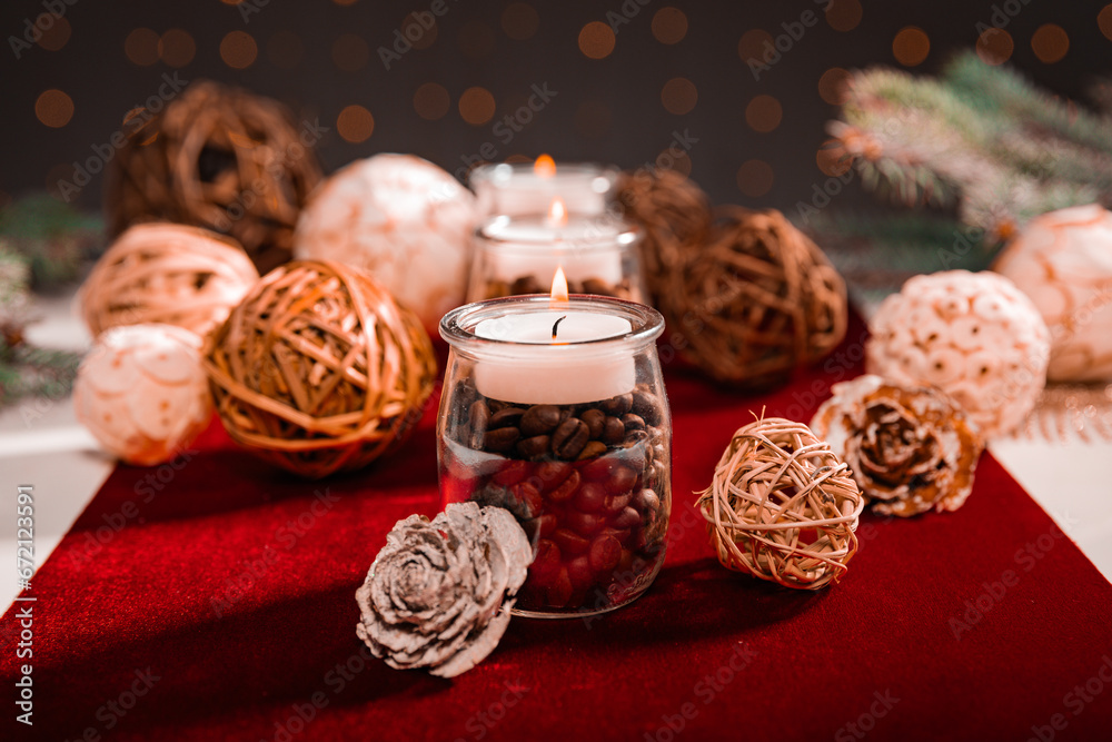 candles standing on wood among white-brown balls with white-red accessories on a dark background and branches of a Christmas tree