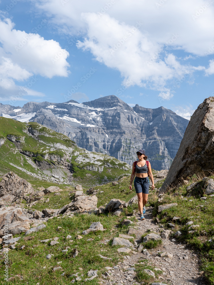 Vertical photo of a young adult woman hiking in a stunning mountainous landscape - concept of a healthy lifestyle, well-being, and hiking.