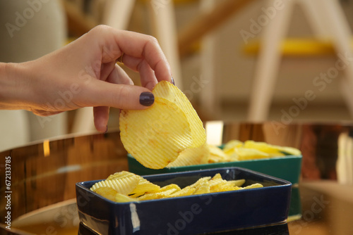 Young sad woman having unhealthy snack, eating potato chips in the livingroom. Junk food and unhealthy eating concept.	 photo