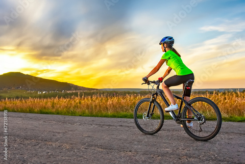 Beautiful woman cyclist riding a bike on the road towards the sunset. Nature and recreation. Hobbies and sports