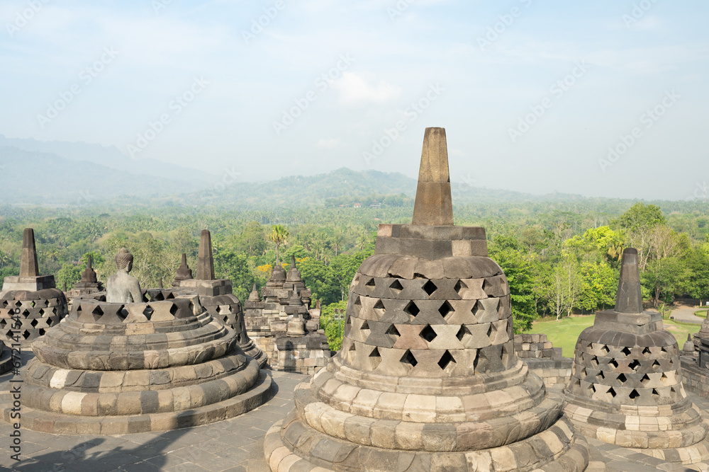 (Selective focus) Stunning view of a Buddha Statue in the foreground and some bell shaped stupas in the background. Borobudur is a Mahayana Buddhist temple in Indonesia.