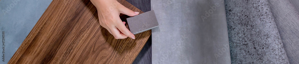 An interior designer's hand selects a palette of sample materials that includes different types, textures and colors of artificial stone, wooden MDF board and decorative wallpaper An interior designer's hand selects a palette of sample materials that includes different types, textures and colors of artificial stone, wooden MDF board and decorative wallpaper