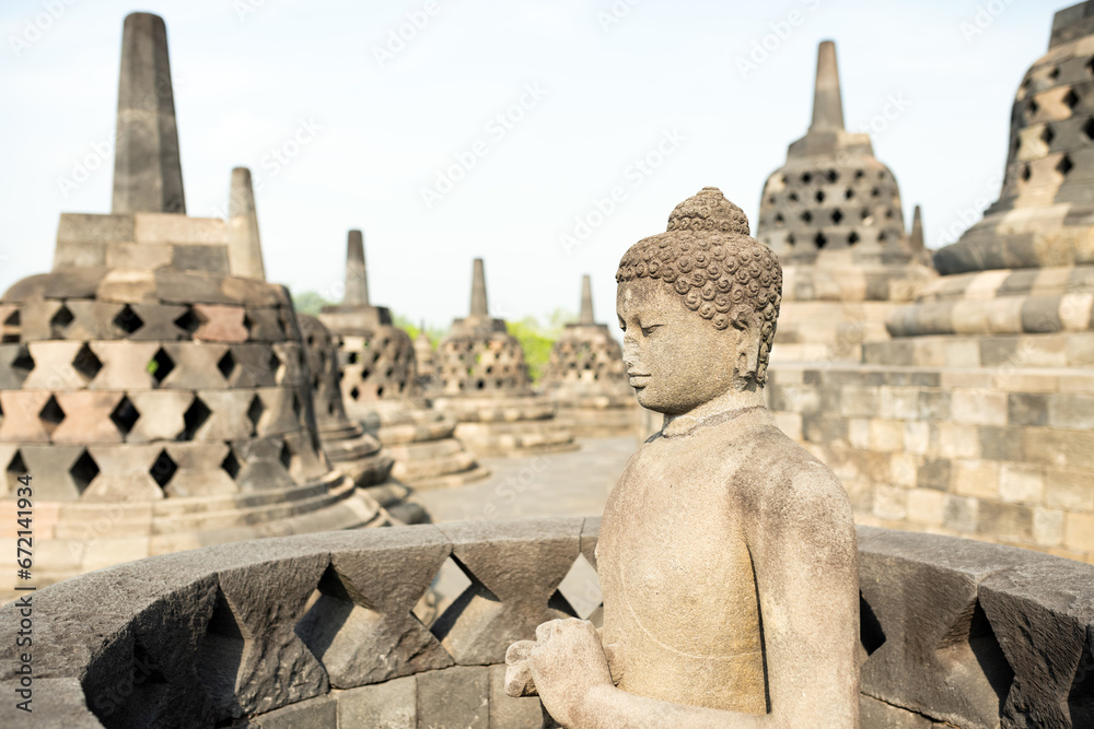(Selective focus) Stunning view of a Buddha Statue in the foreground and some bell shaped stupas in the background. Borobudur is a Mahayana Buddhist temple in Indonesia.