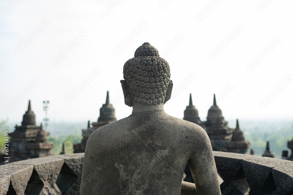 (Selective focus) Stunning view of a Buddha Statue in the foreground and some bell shaped stupas in the background. Borobudur is a Mahayana Buddhist temple in Indonesia.