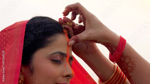 Closeup shot of a woman applying sindoor in a ritual for Chhath Pooja - religious festival  offering prayer to Lord sun. Beautiful young woman celebrating the festival of Chhath Pooja in the mornin... photo